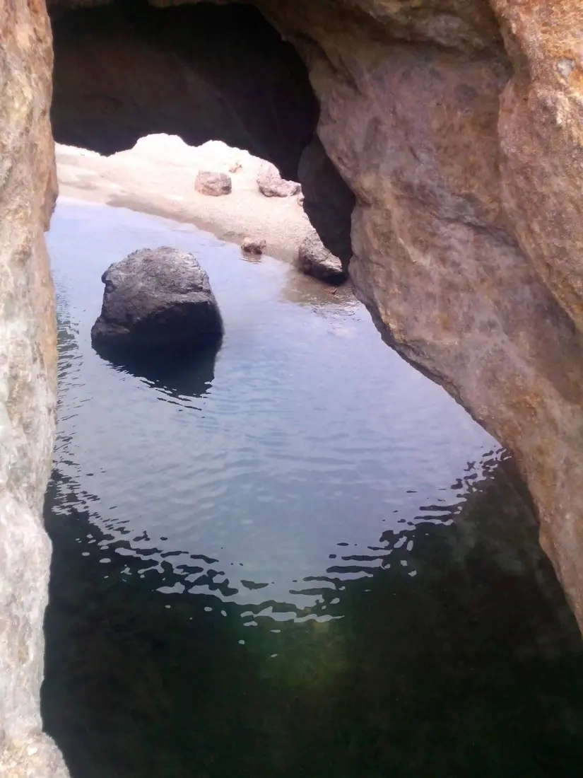 Bajo el arco de roca esta un acantilado sereno en la playa Arquitos Foot: Senderismo kids Aventuras, con Paulina (Facebook)