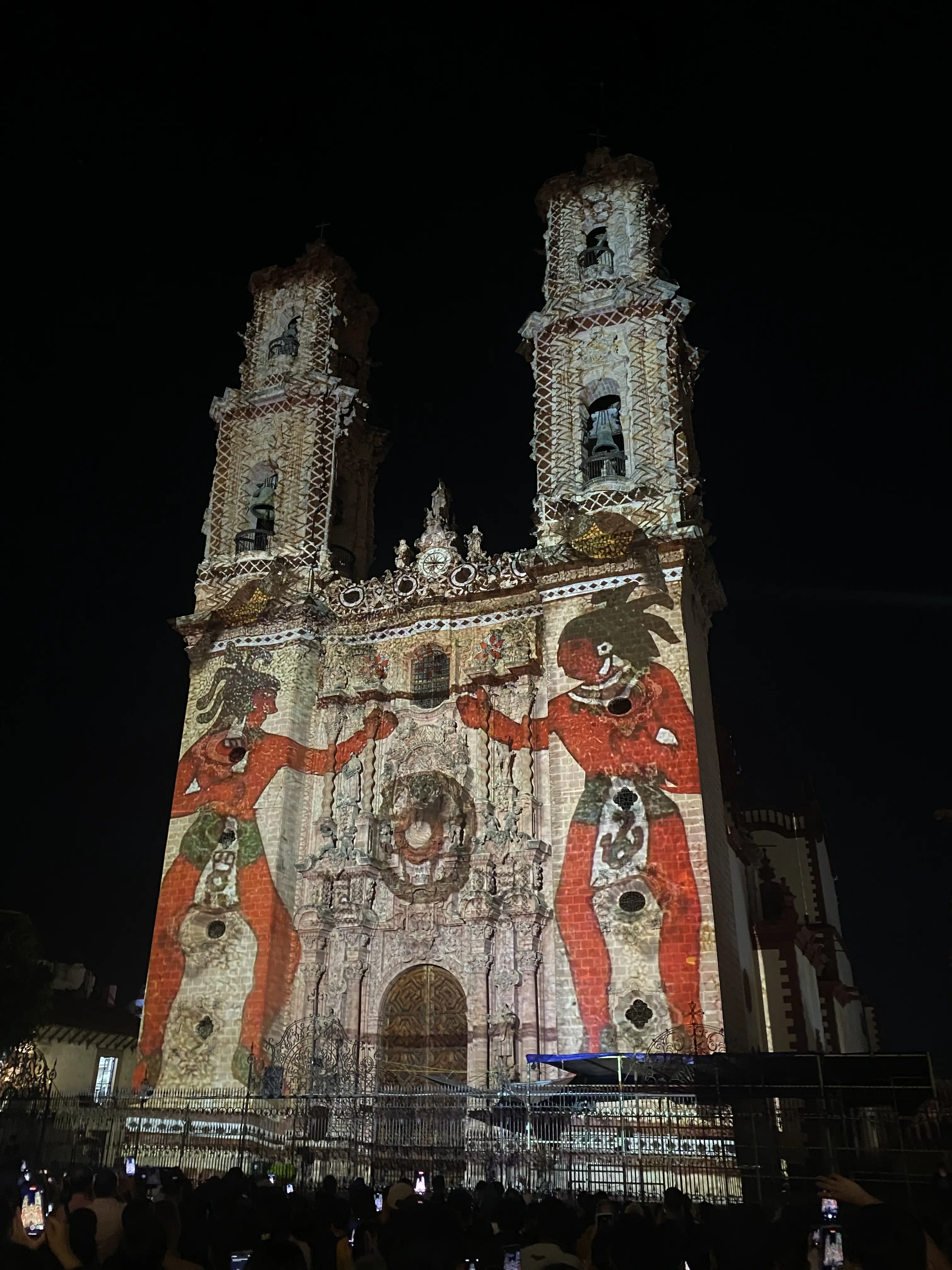  La parroquia de Santa Prisca iluminada de noche, uno de los máximos referentes arquitectónicos y espirituales de Taxco. Al frente, una figura prehispánica representa el sincretismo de esta ciudad. Foto: Hugo Quinto Gutiérrez