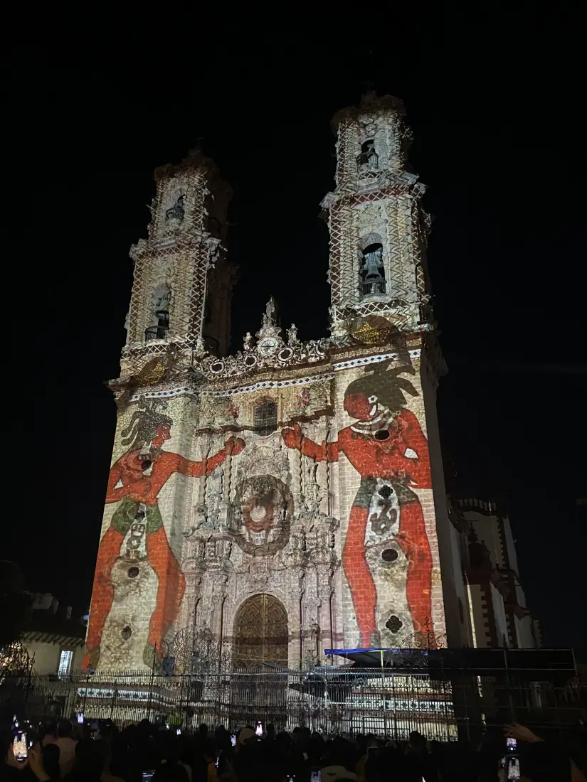  La parroquia de Santa Prisca iluminada de noche, uno de los máximos referentes arquitectónicos y espirituales de Taxco. Al frente, una figura prehispánica representa el sincretismo de esta ciudad. Foto: Hugo Quinto Gutiérrez