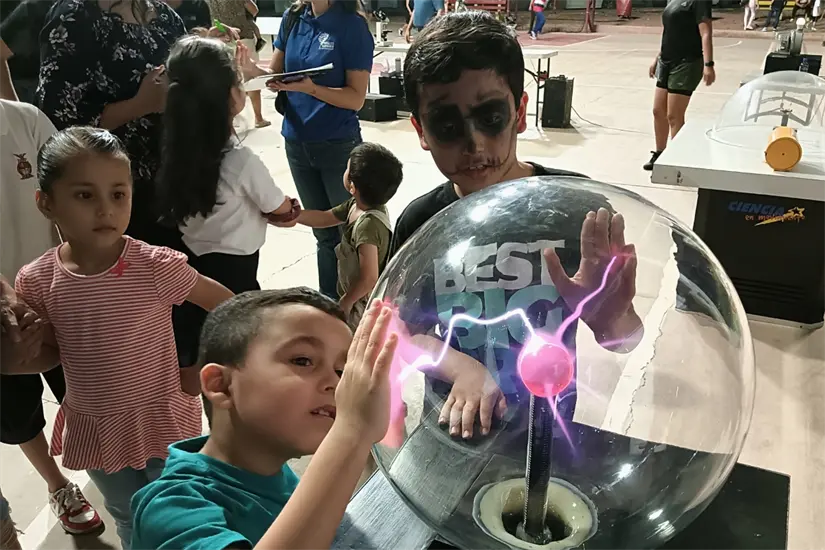 Momento en que un par de niños observan el efecto de la conductividad eléctrica en la esfera de plasma, una luminosa esfera de cristal. 