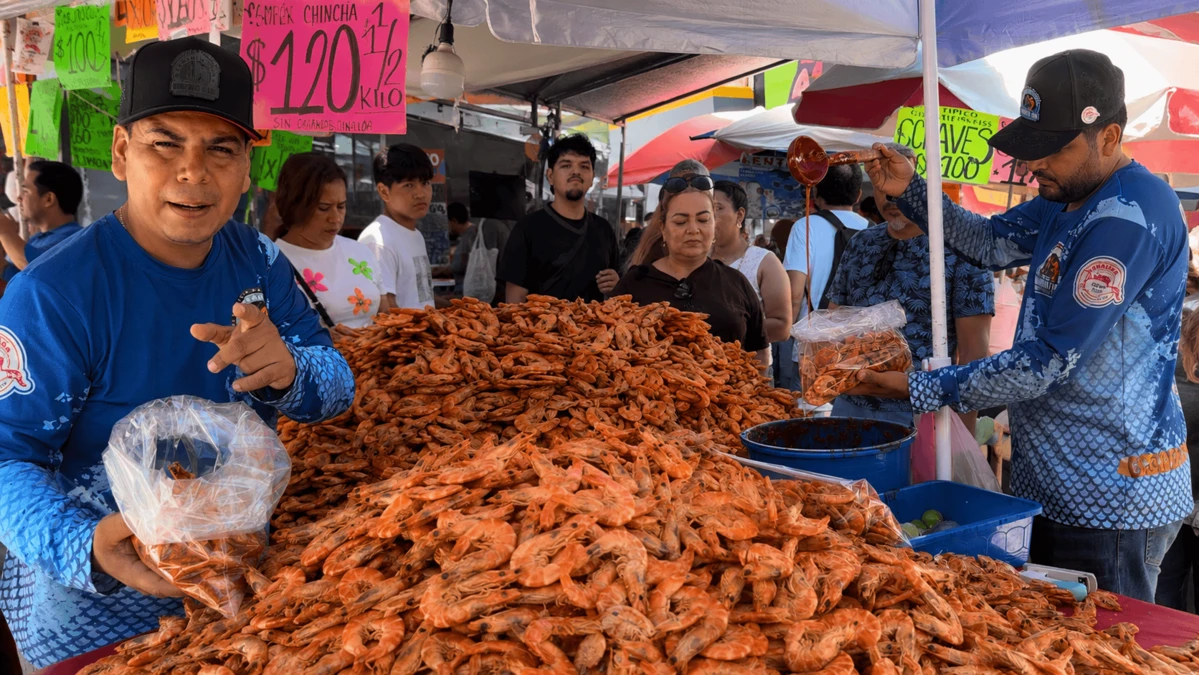 Erick Flores continúa el legado familiar en uno de los puestos más tradicionales del Centro de Mazatlán, donde locales y turistas disfrutan del famoso camarón seco y aprovechan para tomarse una fotografía con él.